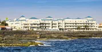 Un hotel frente al mar con varios balcones, un litoral rocoso y vistas al océano.