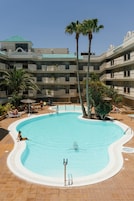 Una piscina rodeada de palmeras y un edificio con varios balcones.