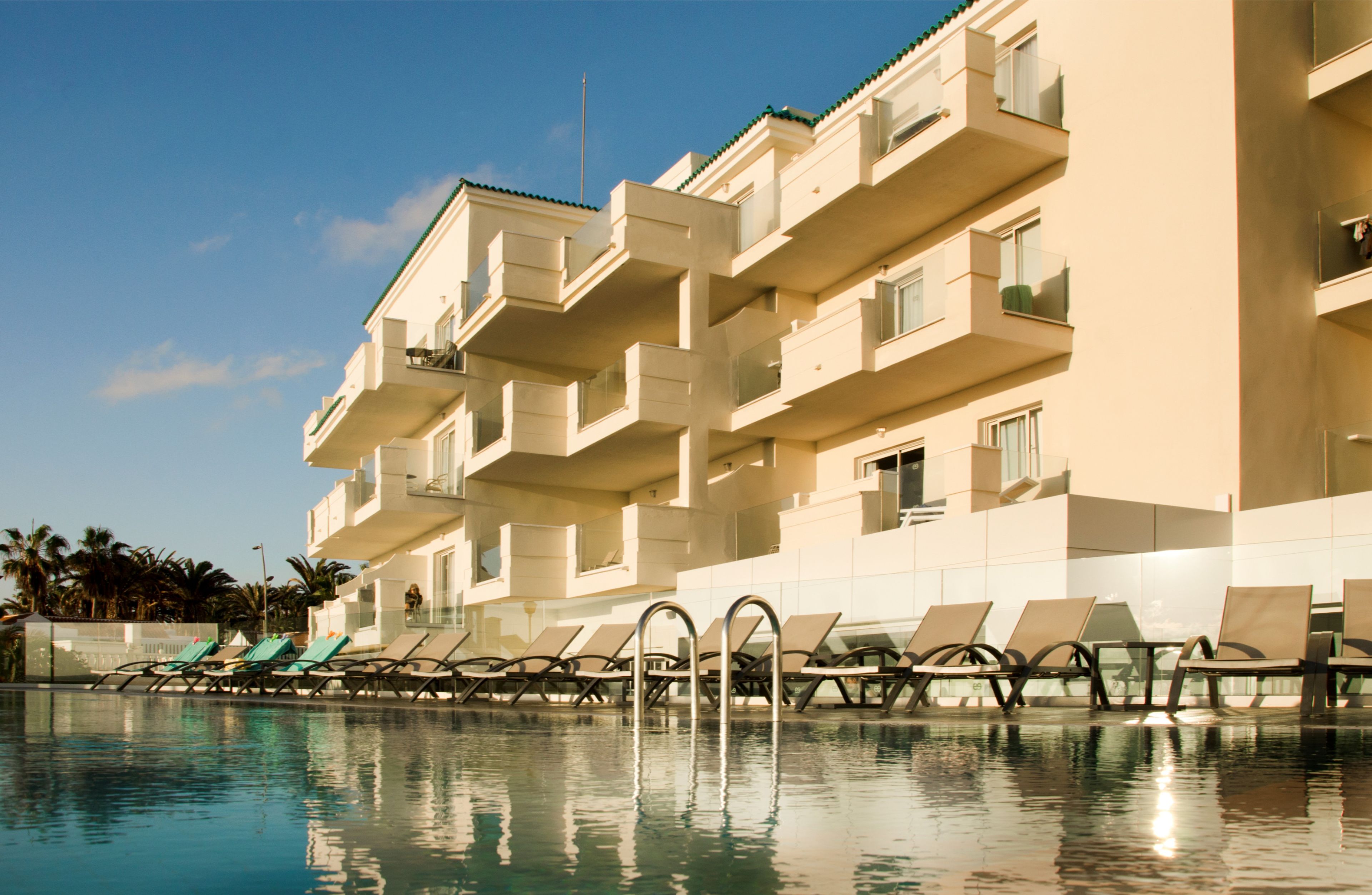 Un hotel con piscina, varios balcones y sillas de descanso.