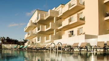 Un hotel con piscina, varios balcones y sillas de descanso.