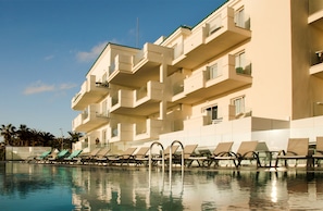 A hotel with a pool, multiple balconies, and lounge chairs. - Hotiday Fuerteventura Seafront (Antigua)