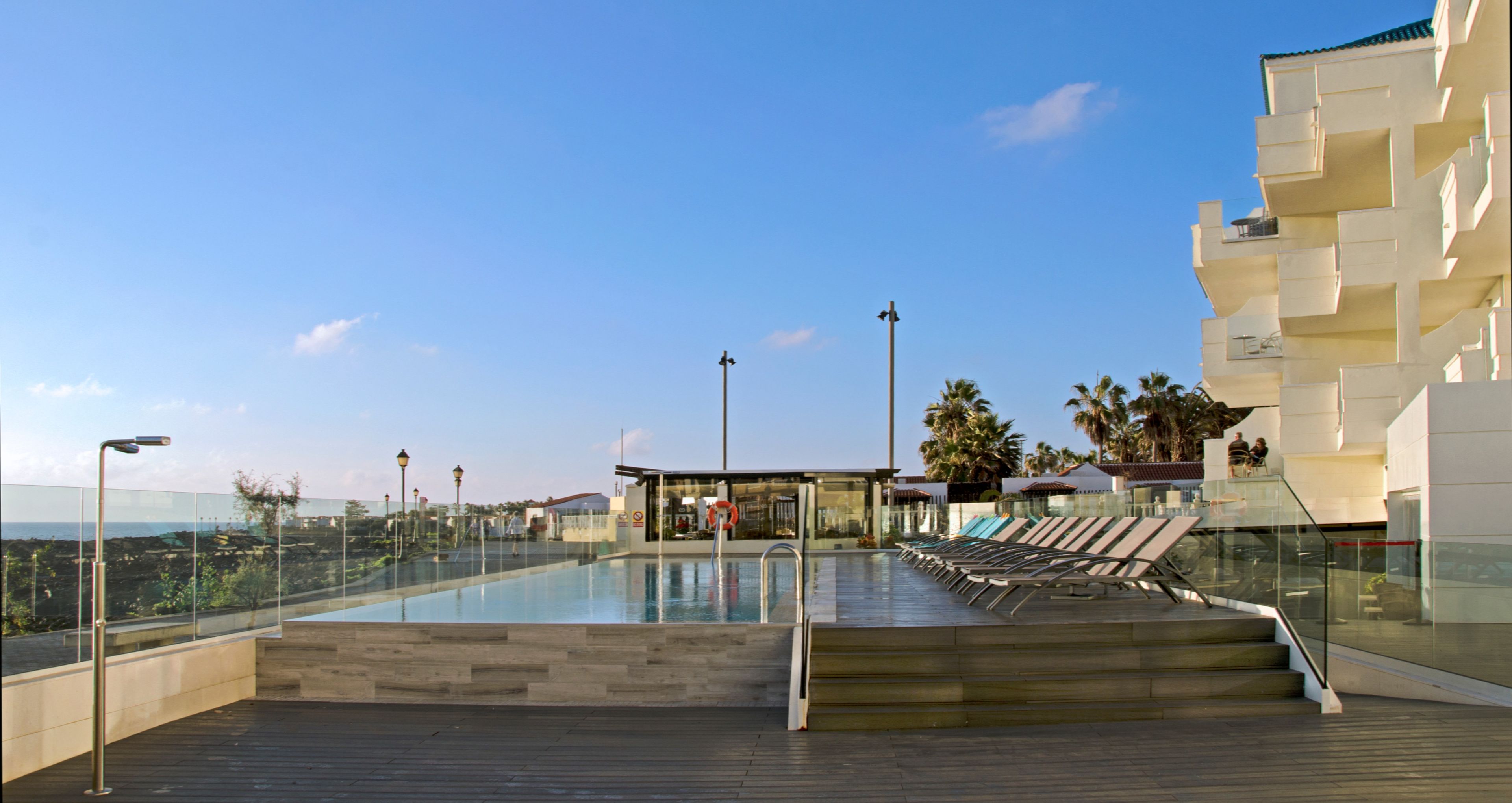 Piscina no terraço com vista clara do oceano, cercada por arquitetura moderna e palmeiras.