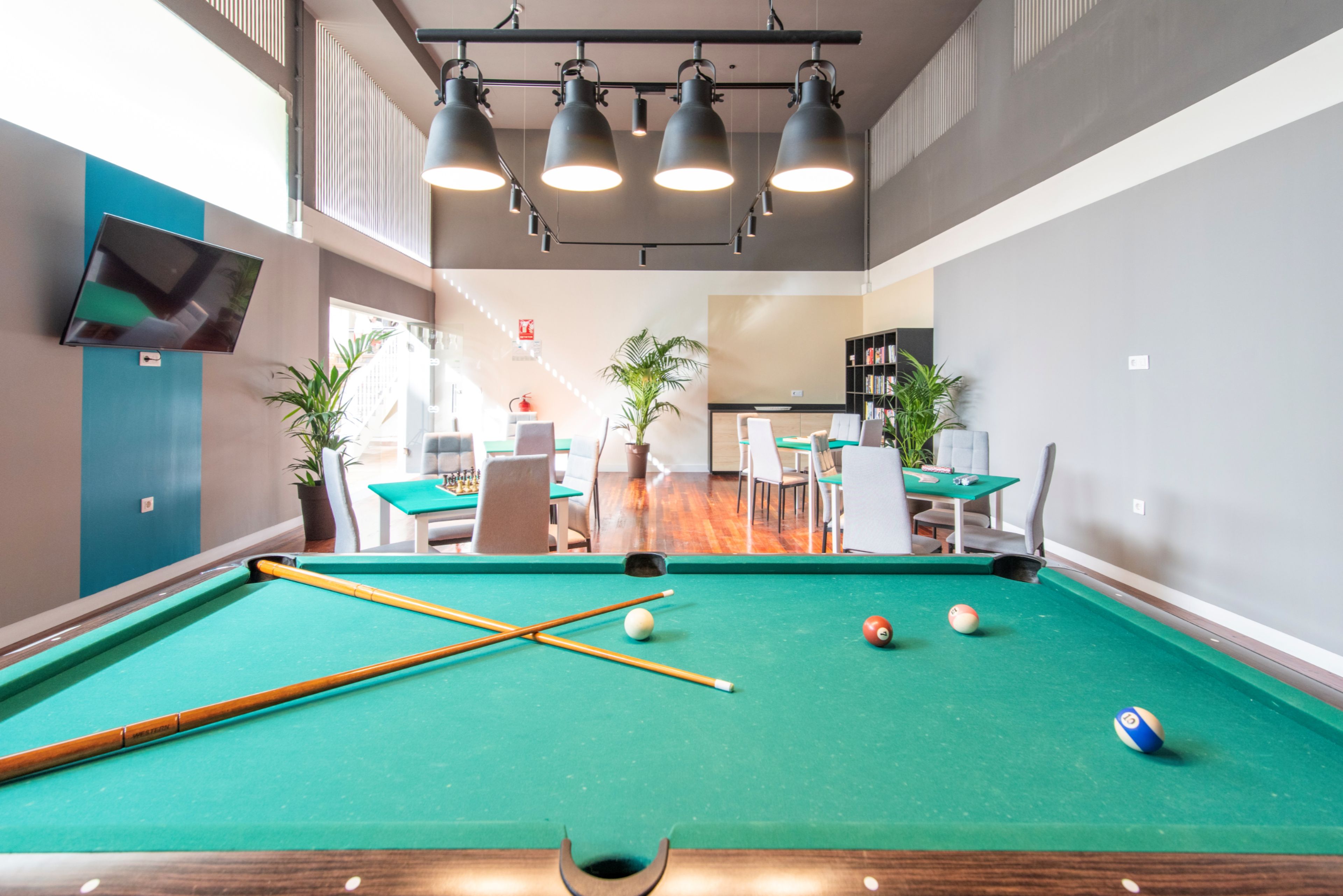 A pool table with balls and cues, a seating area with tables and chairs, and a bookshelf in a room with a modern design.