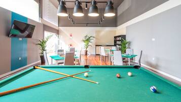 A pool table with balls and cues, a seating area with tables and chairs, and a bookshelf in a room with a modern design.