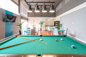 A pool table with balls and cues, a seating area with tables and chairs, and a bookshelf in a room with a modern design.