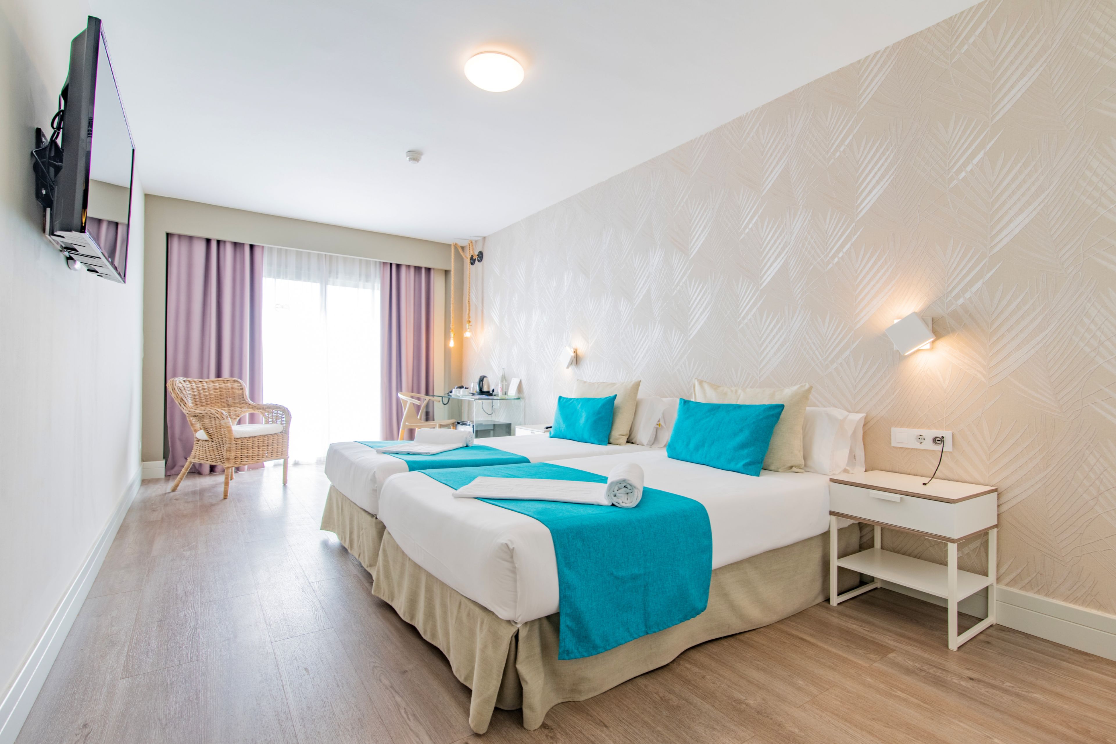 A hotel room with two beds, a desk, a chair, and a television.