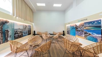 Een modern ingerichte vergaderruimte met een houten vloer, rieten stoelen en wanddecoratie met afbeeldingen van kustlandschappen.