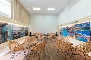 Un salón de conferencias con diseño moderno, que presenta piso de madera, sillas de mimbre y obras de arte colgantes con paisajes costeros.