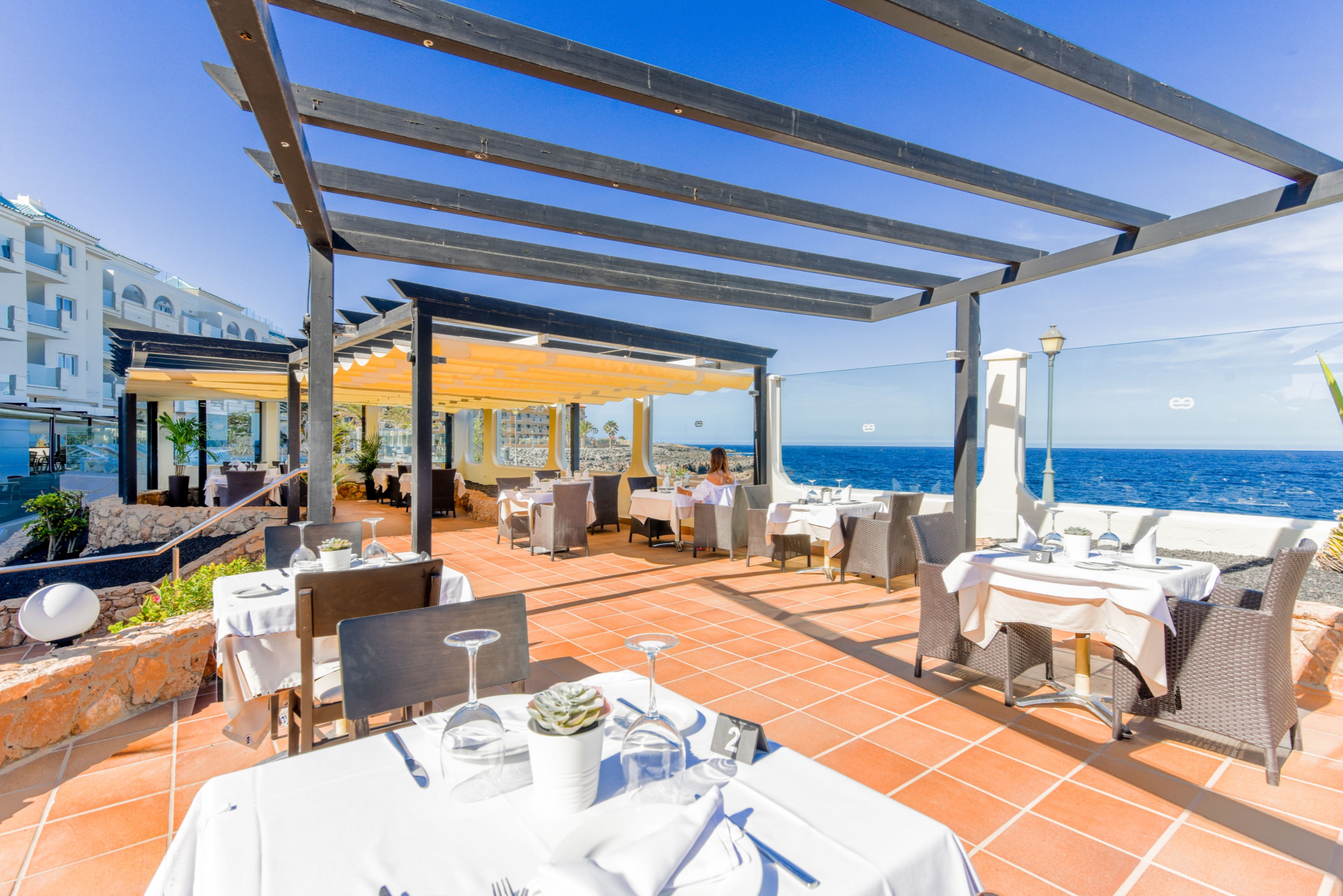Een terras buiten met tafels en stoelen, met uitzicht op zee.