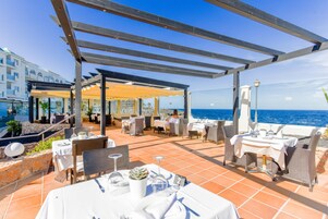 Una terraza al aire libre con mesas y sillas, con vistas al mar.