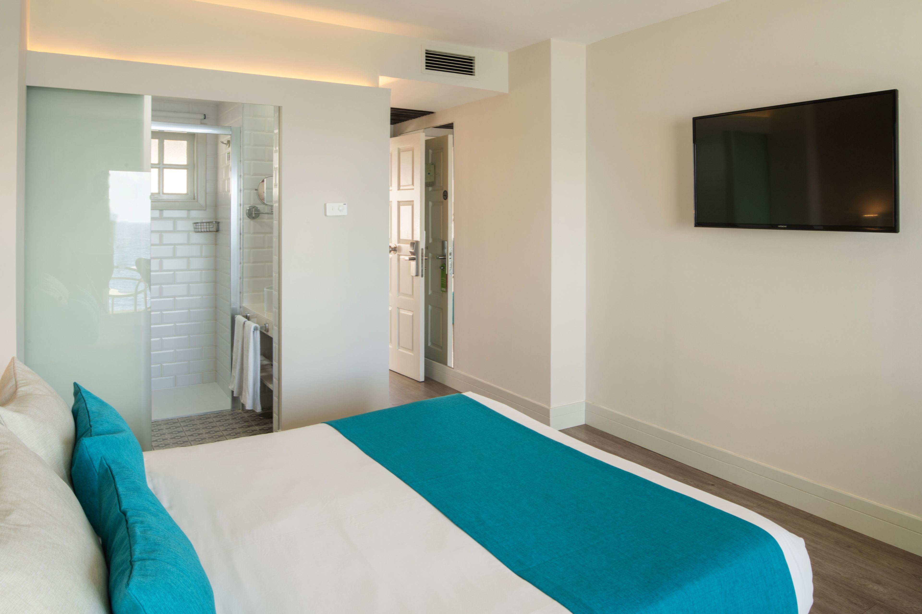 A hotel room with a bed, a TV mounted on the wall, and a bathroom visible through an open door.