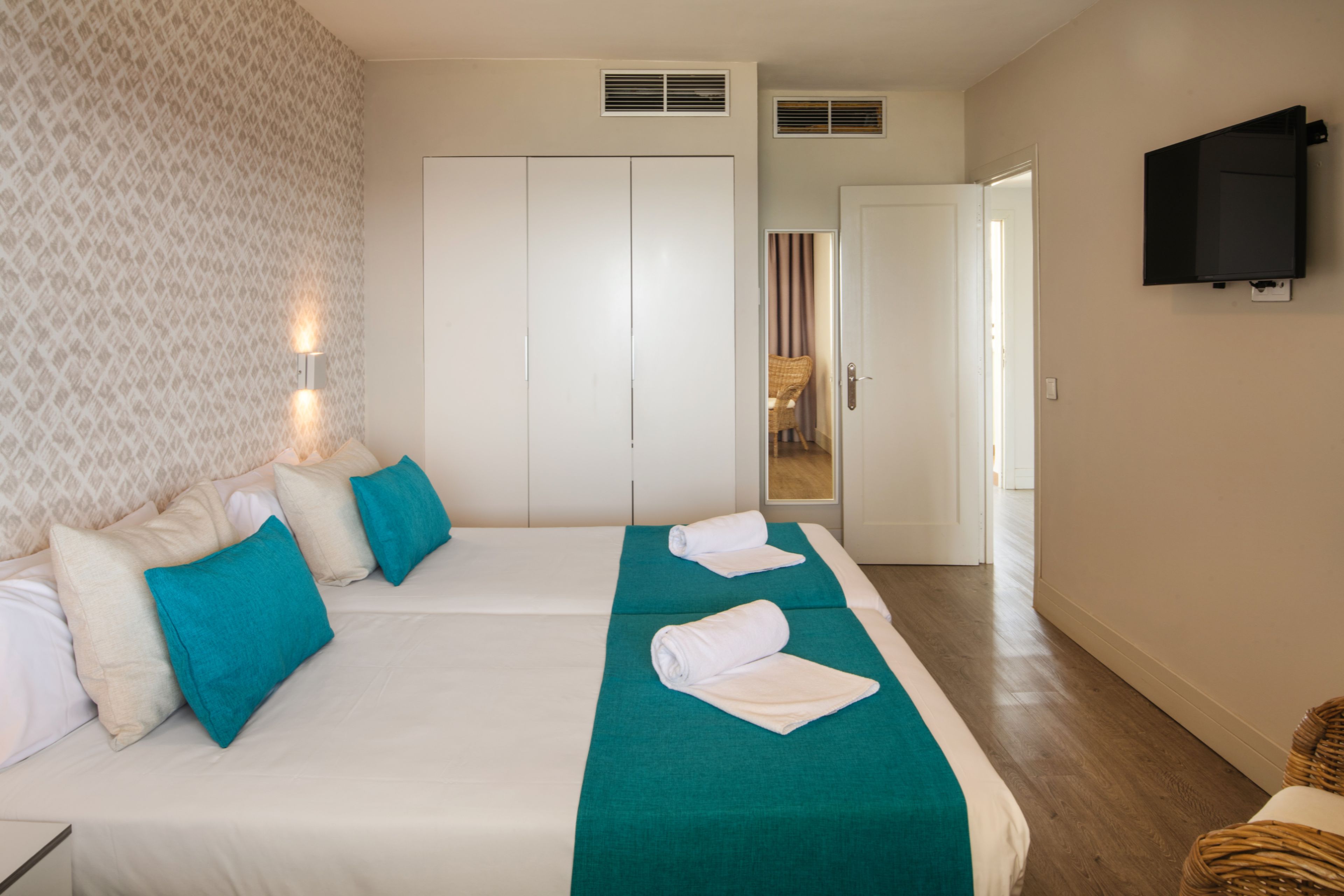 A hotel room with a large bed, a television mounted on the wall, and a wardrobe.
