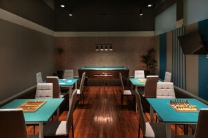 Un salón de conferencias con mesa de billar, dos mesas de ajedrez y una pared de ladrillo.