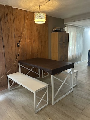 A dining area with a wooden wall, a hanging light fixture, and a table with benches. - Suwannee River Canopy Cabin - 5 Min Walk to Gornto Springs - Wetland Bridge View (Old Town)