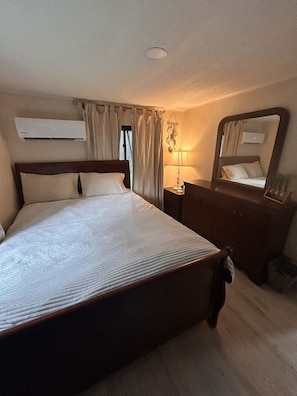 A hotel room with a large bed, a dresser, a mirror, an air conditioning unit, and curtains. - Suwannee River Canopy Cabin - 5 Min Walk to Gornto Springs - Wetland Bridge View (Old Town)