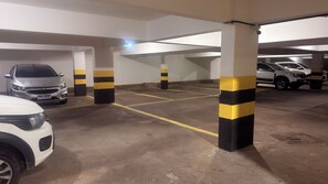 A parking garage with concrete pillars, yellow and black striped columns, and cars parked. - Beachfront apartment for rent on Avenida beach. (Maceió)