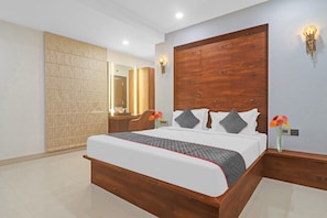 A modern hotel room with a large bed, wooden headboard, a mirror, and a wall-mounted light fixture.