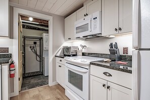 A compact kitchen with white cabinetry, a built-in microwave, a stove, and a sink. - Stonewall Flat in-town Bethel (Bethel)
