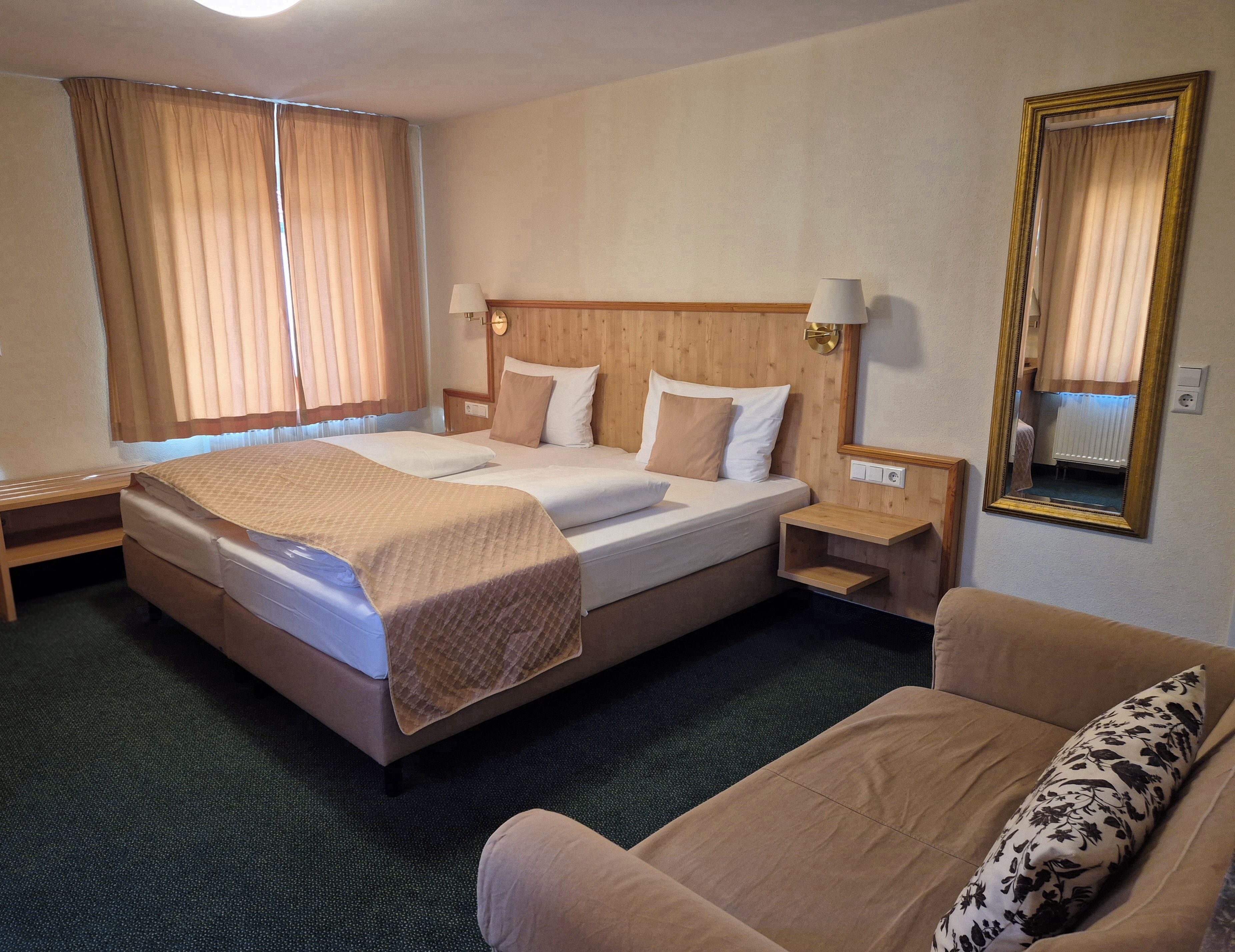Een hotelkamer met een bed, nachtkastjes, een stoel, een spiegel en gordijnen.