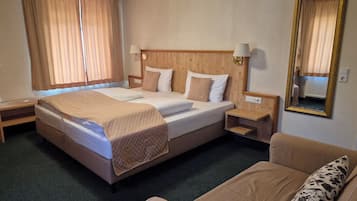 Een hotelkamer met een bed, nachtkastjes, een stoel, een spiegel en gordijnen.