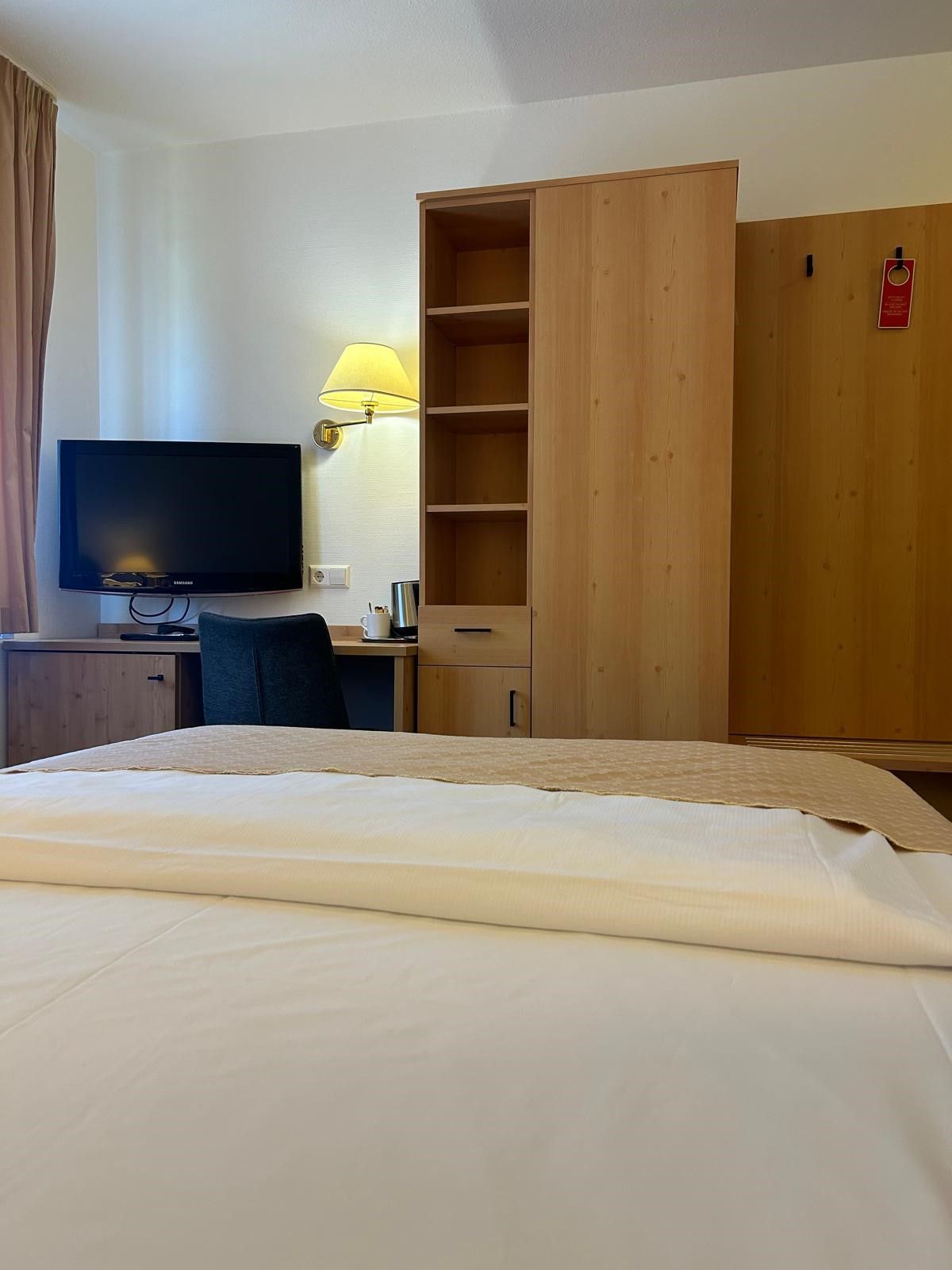 Ein Hotelzimmer mit Bett, Schreibtisch mit Lampe, Fernseher und Kleiderschrank.