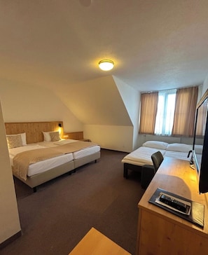 A hotel room with a bed, a desk, and a chair. There is a ceiling light and a window with curtains.