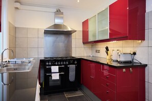 A modern kitchen with a stainless steel range hood, a built-in oven, and red cabinetry. - Belsize Park Scarlet Edit (London)