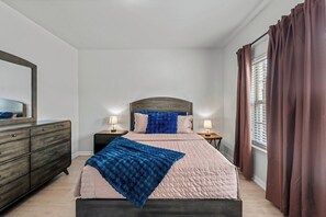 Ein Schlafzimmer mit einem Bett, zwei Nachttischen, einer Kommode und einem Fenster mit Vorhängen.