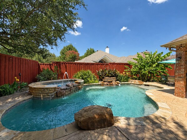 Un jardin avec une piscine, un jacuzzi et une cascade artificielle en pierre.