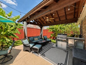 Une terrasse extérieure dotée d’un espace salon couvert, d’un barbecue et d’une pergola illuminée de guirlandes lumineuses.