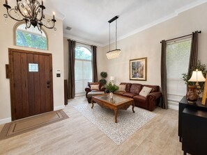 A spacious living room with a wooden door, a chandelier, a sofa set, a coffee table, and a painting on the wall. - 30 Day Rental | Spacious Home with Private Pool | Near Grapevine Lake (Flower Mound)