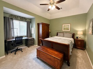 Une chambre à coucher comprenant un lit, un bureau, une chaise, une armoire et un ventilateur de plafond.