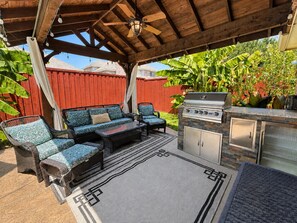 An outdoor patio with a grill, seating area, and a red fence. - 30 Day Rental | Spacious Home with Private Pool | Near Grapevine Lake (Flower Mound)