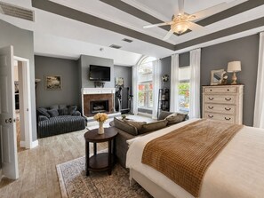Une chambre à coucher avec un grand lit, une cheminée, un téléviseur et une vue sur l’extérieur.
