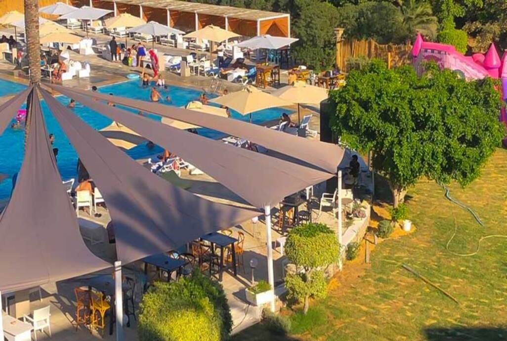 Zona de piscina con múltiples tumbonas y sombrillas, rodeada de vegetación y una estructura que recuerda a un castillo.