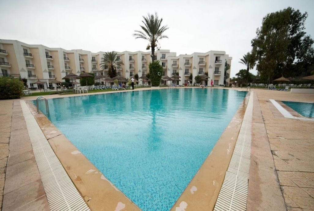 Una piscina rodeada por un edificio con balcones y palmeras.
