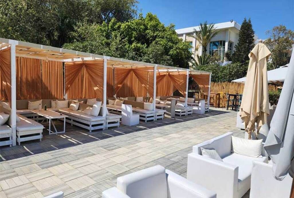 Een overdekt terras met witte lounge fauteuils en een betegelde vloer.