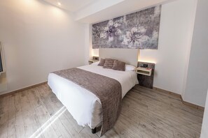 A hotel room with a large bed, a headboard with a floral artwork, bedside tables with lamps, and a wooden floor. - Hotiday Dormelletto Lago (Borgomanero)
