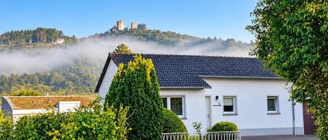 Una casa bianca con tetto scuro, immersa nel verde e sotto un cielo sereno.