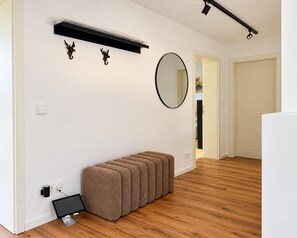 Ein modernes Zimmer mit Holzboden, einer Bank, einem Flachbildfernseher, einem wandmontierten Spiegel und einem Regal mit Dekoration.