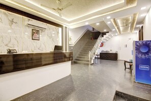 A hotel reception area with a marble reception desk, a staircase, and a wall-mounted refrigerator. - Room-newdelhi Hotel Citizen (New Delhi)