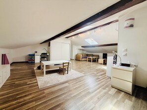 Un loft spacieux avec un plafond haut, une lucarne, un coin repas avec une table et des chaises, un canapé, une petite télévision et un bureau avec un ordinateur.