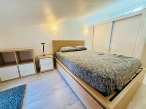 Une chambre à coucher comprenant un lit, une table de chevet, une lampe et un meuble de rangement intégré.