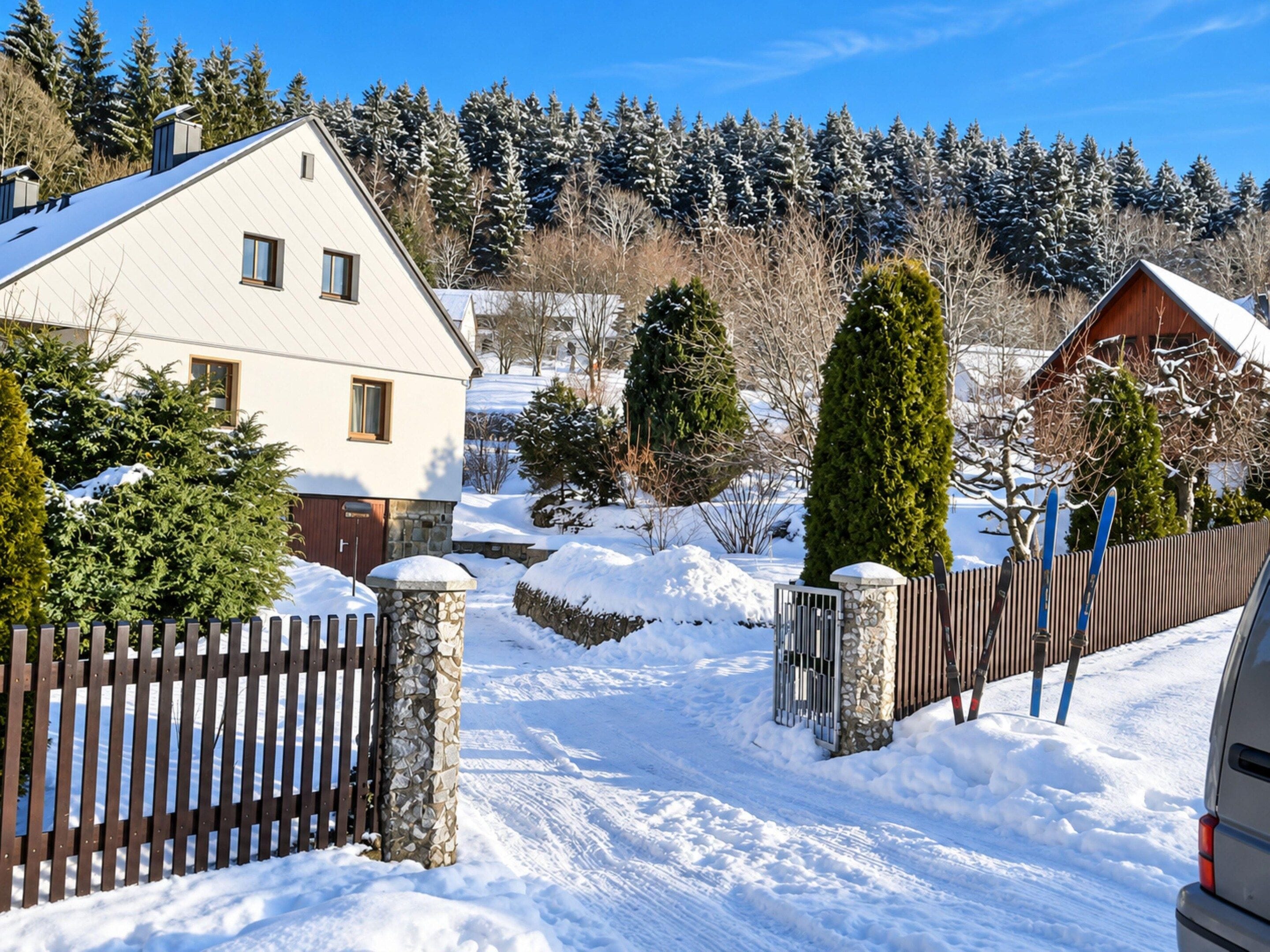 Área residencial coberta de neve, com casas, cerca de madeira e portão de pedra.