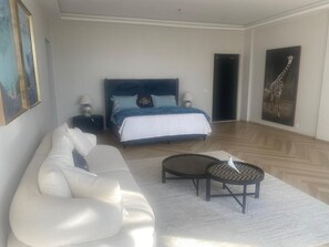 A modern bedroom with a large bed, a white sofa, a small table, and a giraffe painting on the wall. - Stunning 5 suite House with Swimming Pool and Lake (Armação dos Búzios)