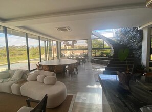 A spacious living area with a large round table, comfortable seating, and a view of the outdoors. - Stunning 5 suite House with Swimming Pool and Lake (Armação dos Búzios)