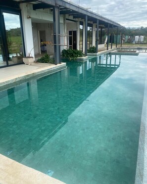 A clear swimming pool with a covered area and potted plants. - Stunning 5 suite House with Swimming Pool and Lake (Armação dos Búzios)