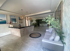 A modern interior with a marble reception desk, a grey sofa, and a dining area with a view. - Stunning 5 suite House with Swimming Pool and Lake (Armação dos Búzios)