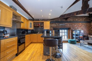 A modern kitchen with wooden cabinets, a black countertop, and a brick wall. - Modern 2-BR Loft Flat W/Parking near Lime St (Liverpool)