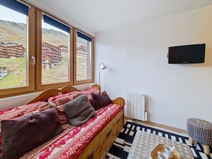 Ein Zimmer mit einer Holzsofa, einem an der Wand befestigten Fernseher und Bergblick durch große Fenster.